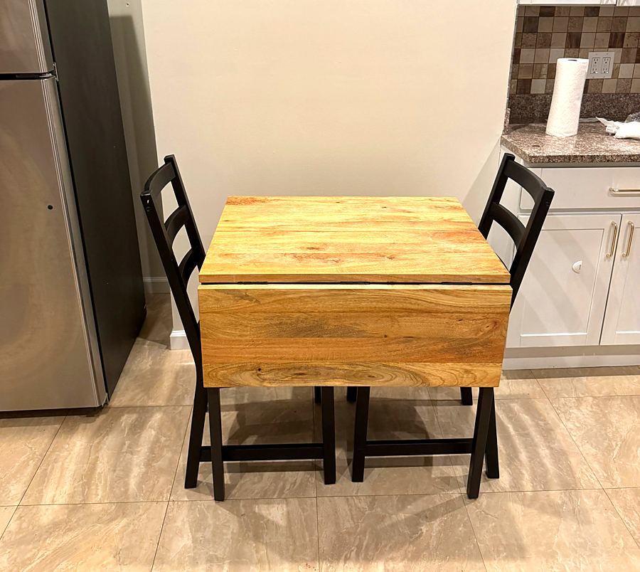 Assembled wooden drop-leaf table with two black chairs in a kitchen